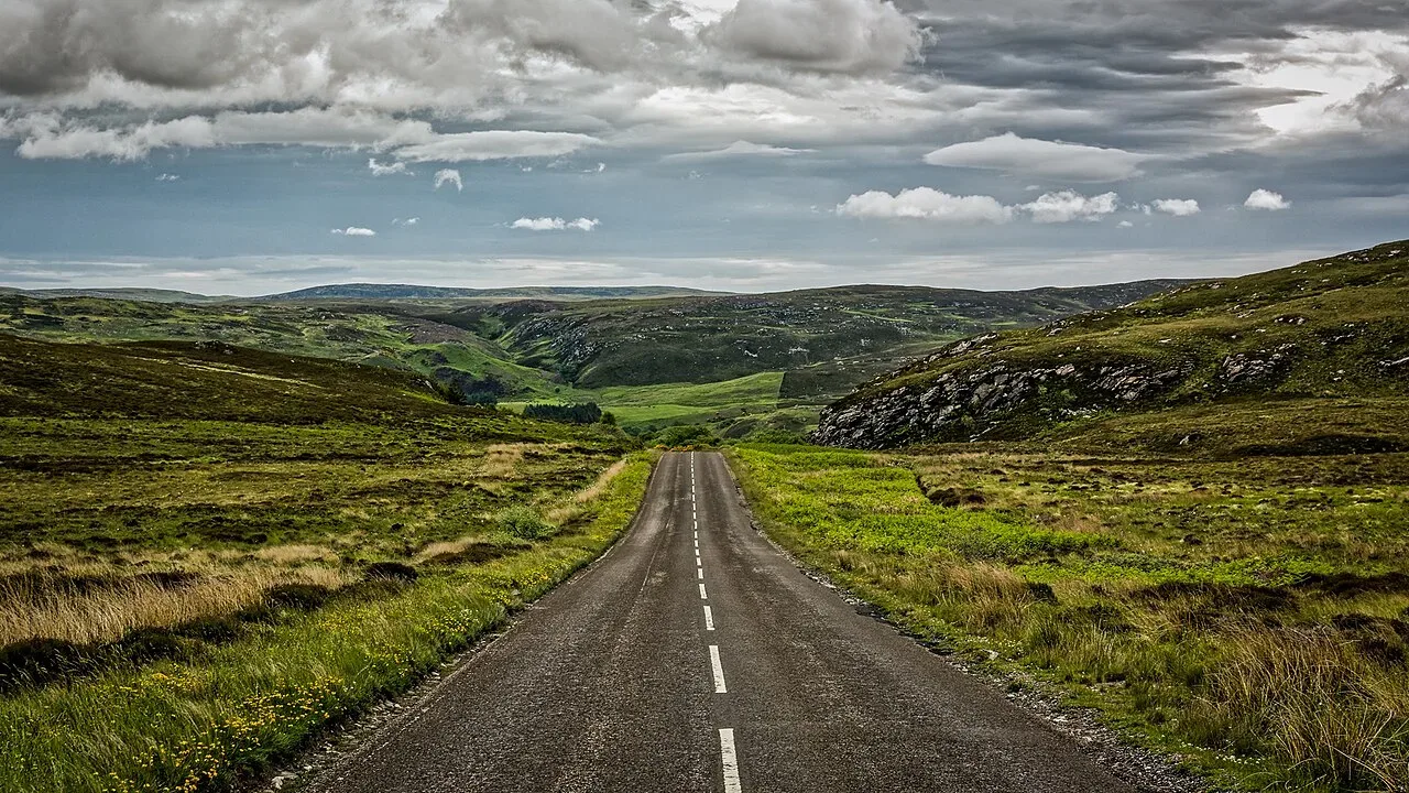 A narrow single-track road winding through the Scottish Highlands